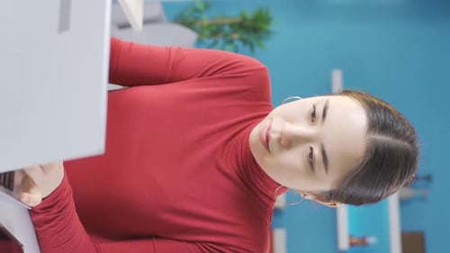 Vertical Video of Young Asian woman looking focused at laptop at home.