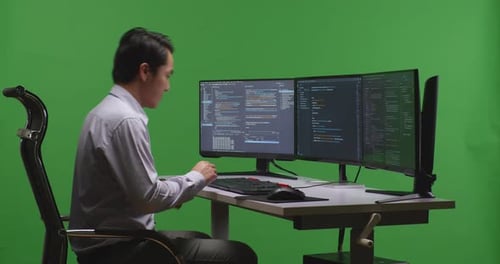 Un homme asiatique s'assoit et travaille avec une maquette de plusieurs écrans d'ordinateur dans un studio à écran vert