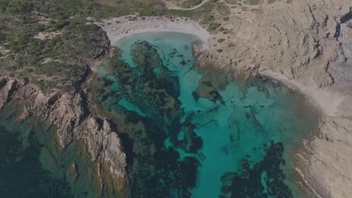 Aerial panoramic natural blue rocky cliff bay forested Cala Sa Torreta Beach Sea in Menorca Spain, t