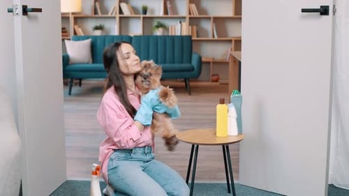 Woman Kneeling Holds Dog With Cleaning Supplies