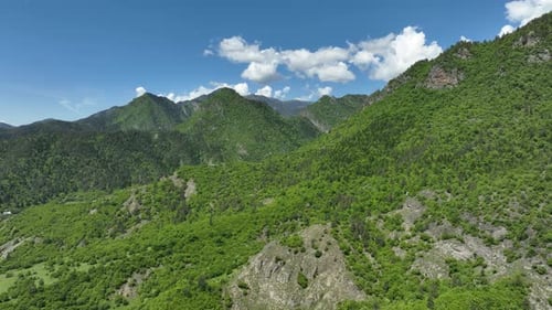 Aerial view of lush green mountain range with dense forest under blue sky and white clouds