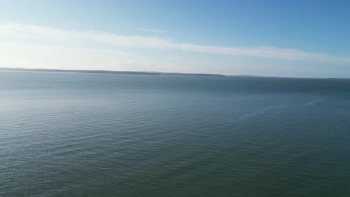 A vast, calm ocean stretches to the horizon under a clear blue sky, with gentle ripples on the water