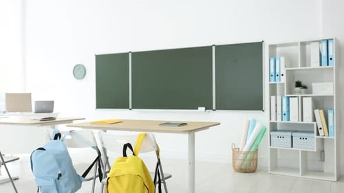 Green chalkboard, backpacks and stylish furniture in classroom. Camera zooming in