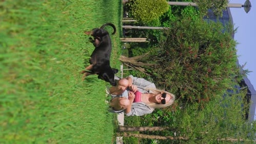 Girl plays with her toy terrier dog in park, she throws ball and dog runs