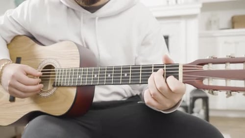 Cropped front view of a young man playing a classical guitar.