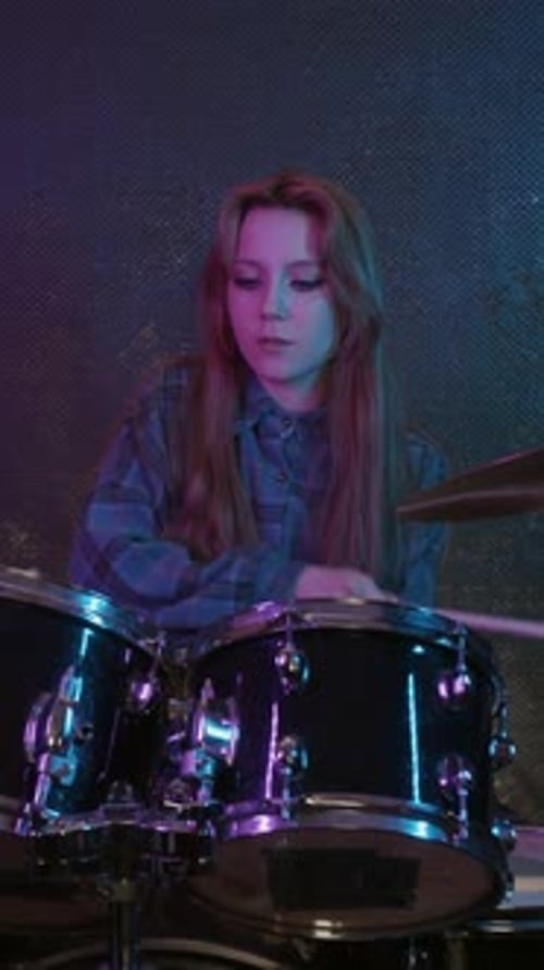 Teenage Girl Plays Drums in Studio with Neon Lighting