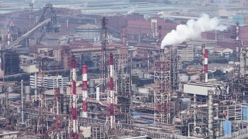 Weitläufiges Industriegebiet mit einem komplexen Netzwerk aus Rohren, Tanks und hohen Schornsteinen, die Rauch abgeben,