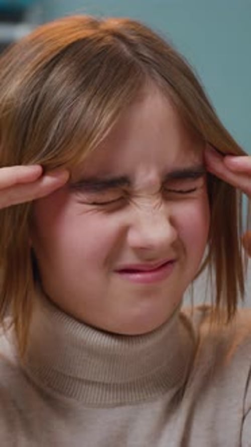 Close Up Face of Tired Preteen Girl Sitting By Table with Headache Massaging Her Temples with