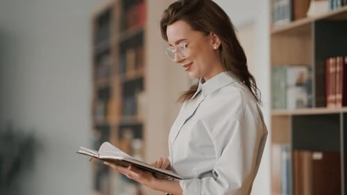 Smiling female student reading a book in the university library