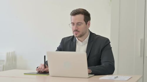 Young Adult Works on Laptop with Tablet
