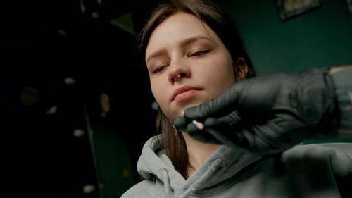 Interior de un estudio de piercings: el maestro de piercings hace un piercing para una niña, piercing para el tabique nasal
