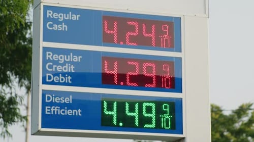 Medium exterior shot of Gas Station Sing with high prices. Trees in the background, late afternoon.