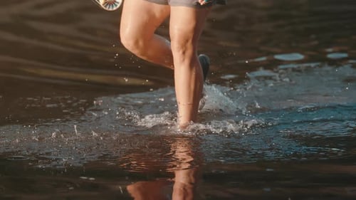 Fly fisherman wading with fishing pole splashing through shallow river in slow motion