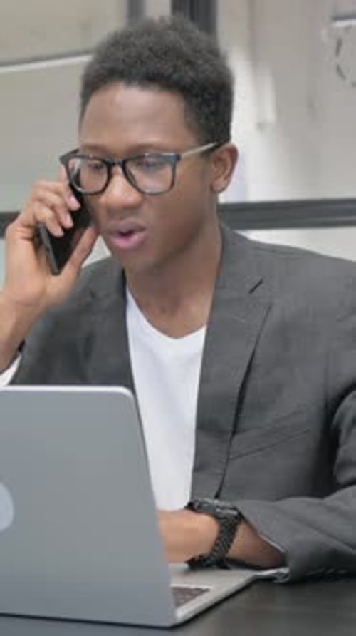Young Man Working On Laptop and Talking on Phone