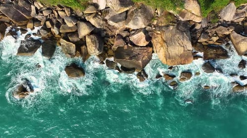 Aerial drone view of foamy waves breaking on a rocky shore.