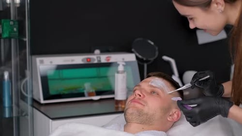 A Cosmetologist Performs a Facial Massage with a Clay Mask Applied to the Face A Man in a Spa
