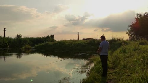 Man On The Riverbank Of Siret River Catching Fish With A Fishing Rod At Dusk. wide shot