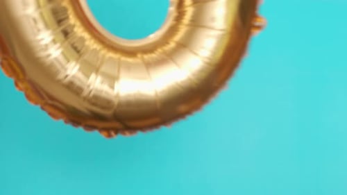Golden Balloon in the Shape of Zero Flies and Falls on Blue Surface at Birthday