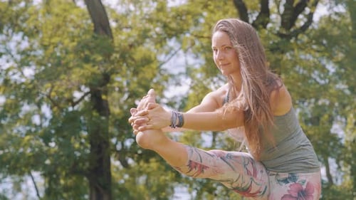 Caucasian woman holds leg yoga pose in nature, slow motion medium shot