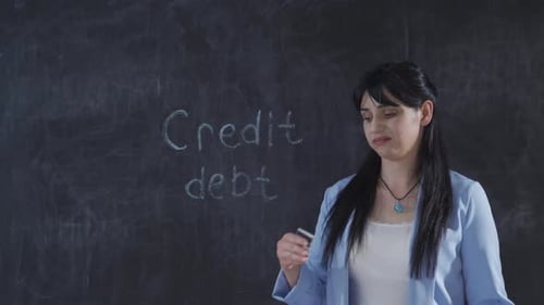The woman writing Loan Debt looks on the blackboard with a sad expression.