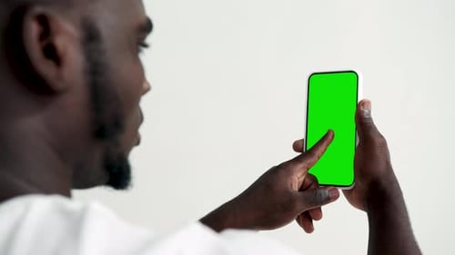 Young man using touchscreen smartphone with green screen chroma key mockup