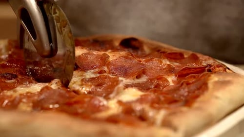 Cutting fresh hot homemade pepperoni pizza into slices - isolated close up of the pizza wheel