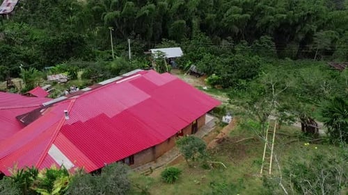 It's a drone shot ascending, showing the red roof of houses in the middle of a forest.