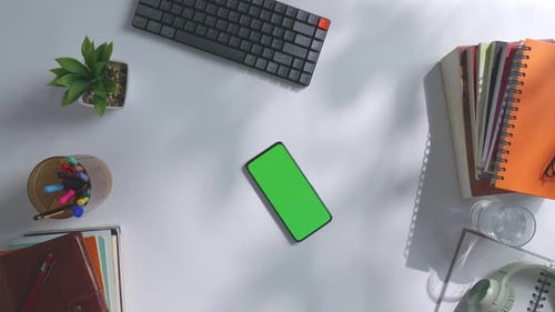 Top down view of a mock up green screen smartphone on a white office desk