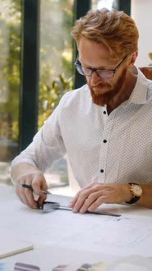 Redhaired Designer Drawing Layout While Sitting in Studio