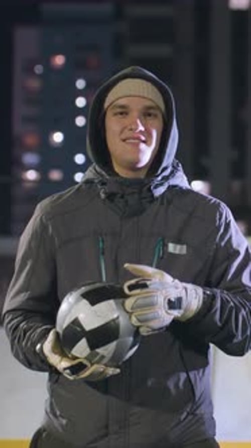 Athlete Smiling While Holding Soccer Ball on Urban Field at Night