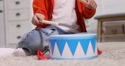 Little boy playing toy drum with drumsticks at home, closeup