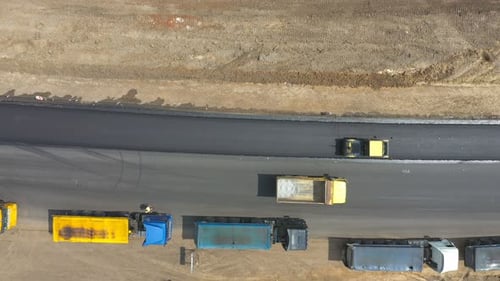 Foto aérea de uma nova estrada de asfalto fabricando rolos e caminhões parados na beira da estrada, máquinas especiais