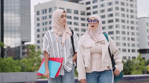Zwei muslimische Studentinnen in Hijabs gehen zusammen auf dem Campus spazieren und reden