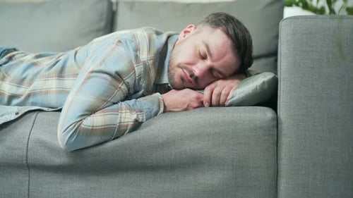 Tired after a hard day, a young Caucasian handsome man is lying on the sofa and resting. Male sleeps