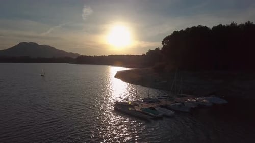 Aerial view of a sunset in a lake with a pier with boats and another sail boat in the water.