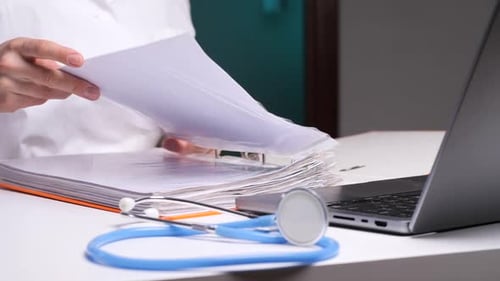 Doctor Reviewing Medical Records in Office with Stethoscope and Laptop
