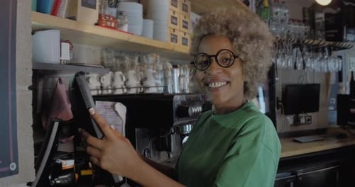Portrait of an African American Waitress in a Pub at the Cash Register Looking at Camera Smiling