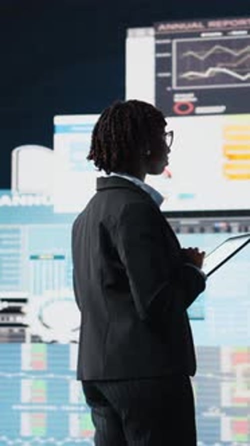 Vertical Video Manager Using Tablet to Compare Company Metrics on Digital Videowall