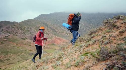 Deux randonneurs grimpent une colline sur un terrain rocheux escarpé dans des conditions de montagne brumeuses et font preuve d'endurance