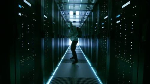 Follow Shot of a Masked Hacker in a Hoodie Running Away with Laptop in a Corporate Data Center.