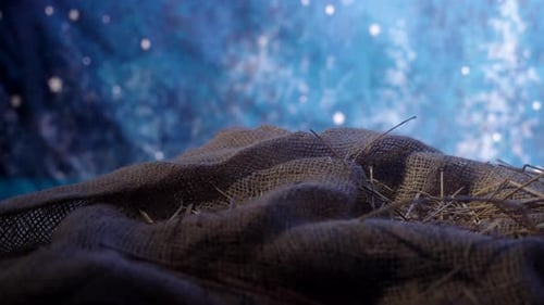 A manger with burlap in hay with starry skies in the background.