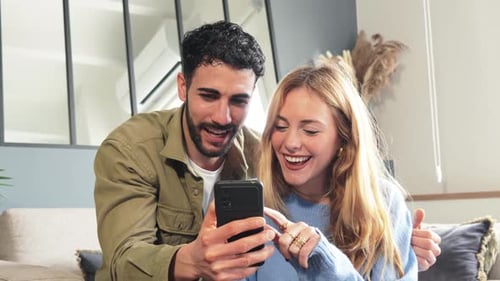 Couple Looking at Phone and Smiling Together Indoors