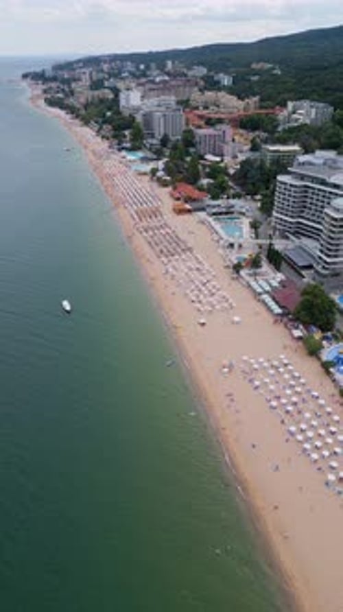 Aerial Shot of a Crowded Beach with Colorful Umbrellas and Swimmers in the Sea Capturing the Essence