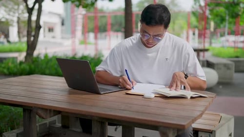 Vergrößern Sie den jungen asiatischen Mann mit Brille, hellbrauner Haut, ernstem Blick, studiert und sich Notizen macht