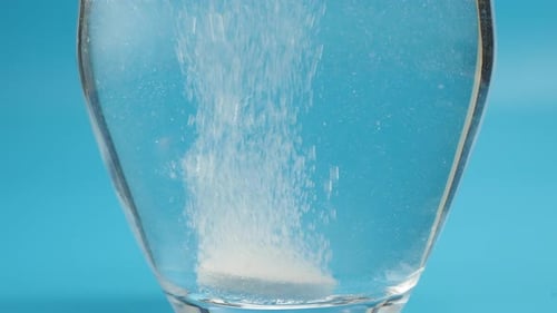 Effervescent tablet in a glass of water close-up on a blue background. Health concept.