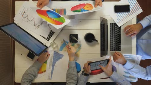 Team Analyzes Data At Table With Charts and Laptops