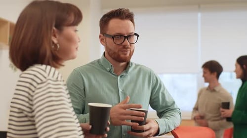 Relaxed Friendly Coworkers Standing in Office Drinking Coffee and Talking Cheerfully in Office Room