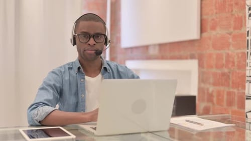 African Call Center Man with headphones Looking toward Camera at Work
