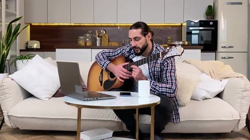 Hombre de mediana edad viendo un Vídeo tutorial para aprender a tocar la guitarra en interiores