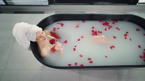 Woman Relaxing in Bath Drinking Wine Blonde Girl Resting Lying in Bath with Warm Milk Rose Petals